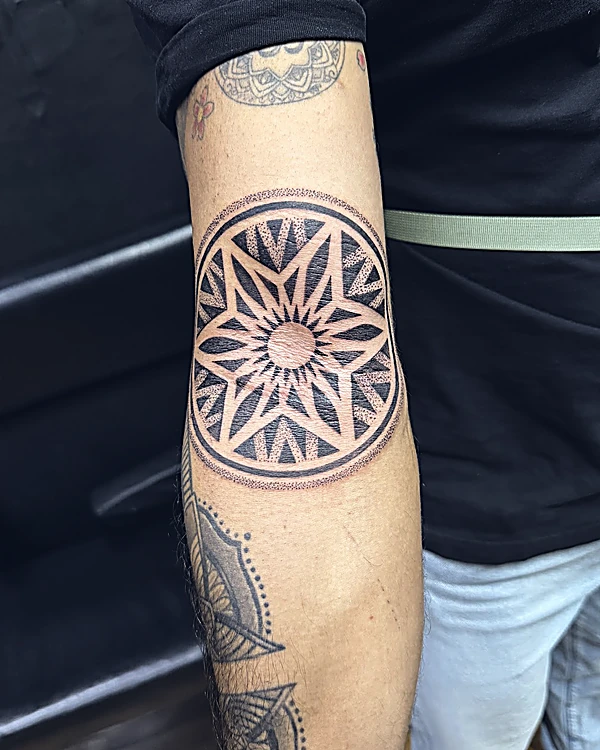 Mandala geométrico de ocho puntas con sombras de puntillismo, tatuado en el codo